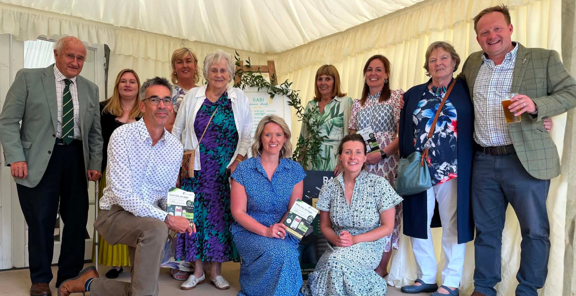 A group of supporters and volunteers pose together inside a marquee at RABI’s County Durham Summer Luncheon fundraiser. Some attendees are standing while others are seated at the front, holding RABI information leaflets. The group smiles for the camera in a welcoming and celebratory atmosphere, reflecting the strong community support behind RABI’s work.