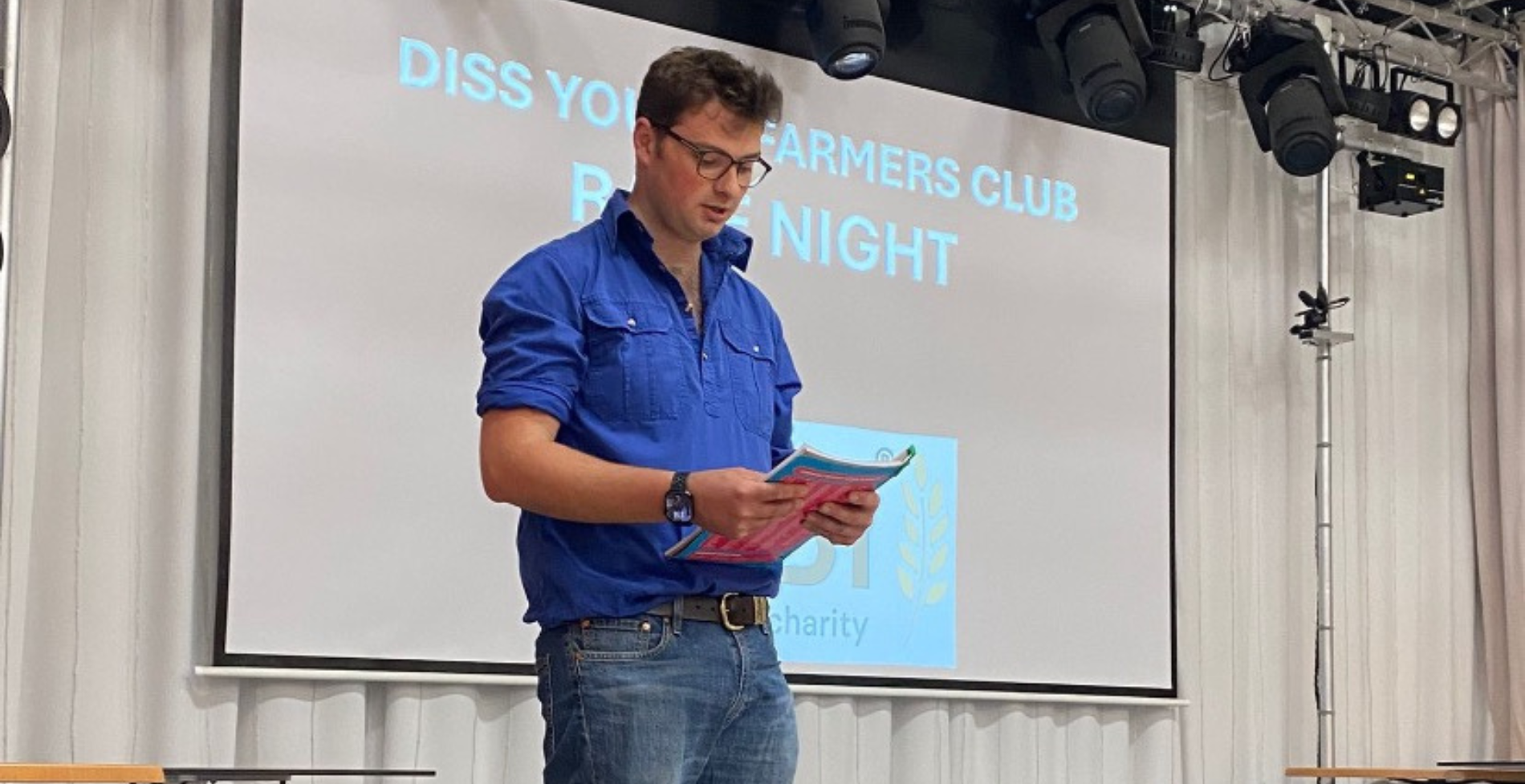 A member of Diss Young Farmers' Club in a blue shirt stood on stage reading notes to a crowd