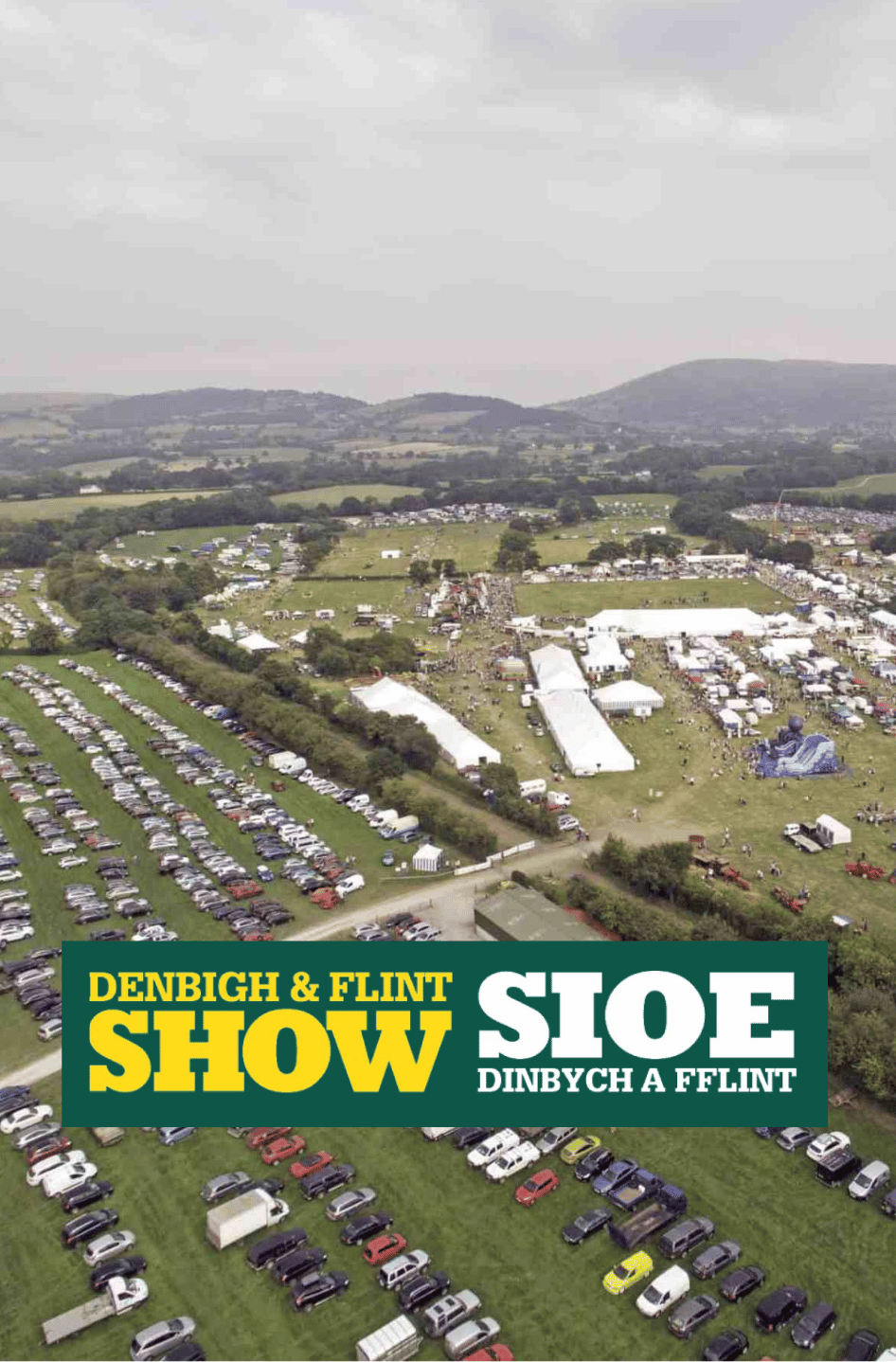 rabi-denbigh-flint-show-2026 Aerial view of the Denbigh & Flint Show, showing the showground, marquees, crowds and surrounding car parks, with the event’s English and Welsh logo.