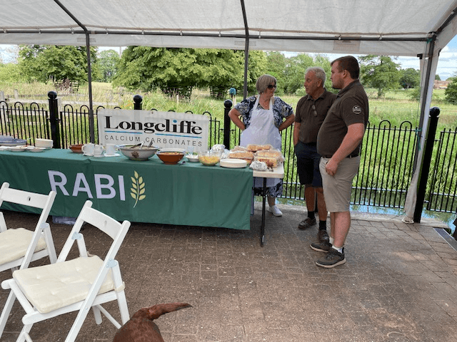 Three people talking beside a RABI-branded refreshment table under a marquee at the RABI Leicestershire Summer Party 2026.