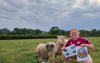 girl crouched down near sheep holding two signs