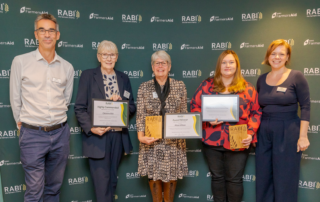 RABI Volunteer Awards recipients and staff standing together with certificates and trophies in front of RABI and FarmersAid branding.