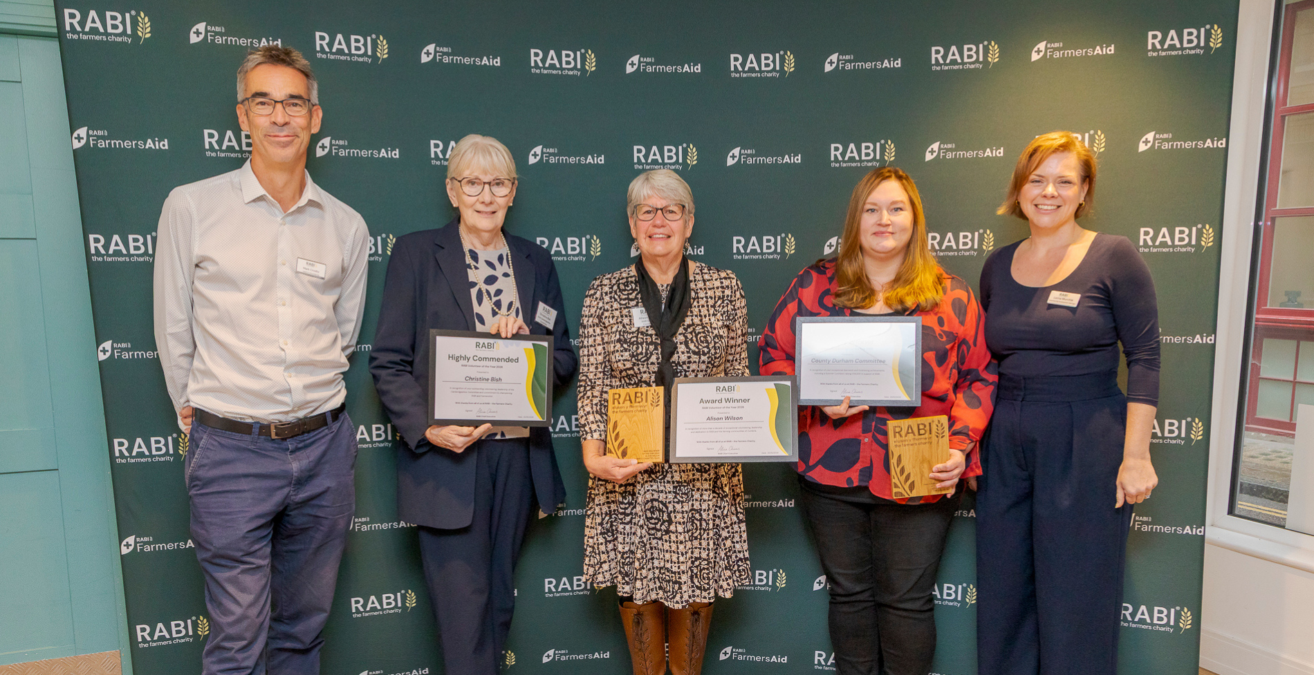 RABI Volunteer Awards recipients and staff standing together with certificates and trophies in front of RABI and FarmersAid branding.