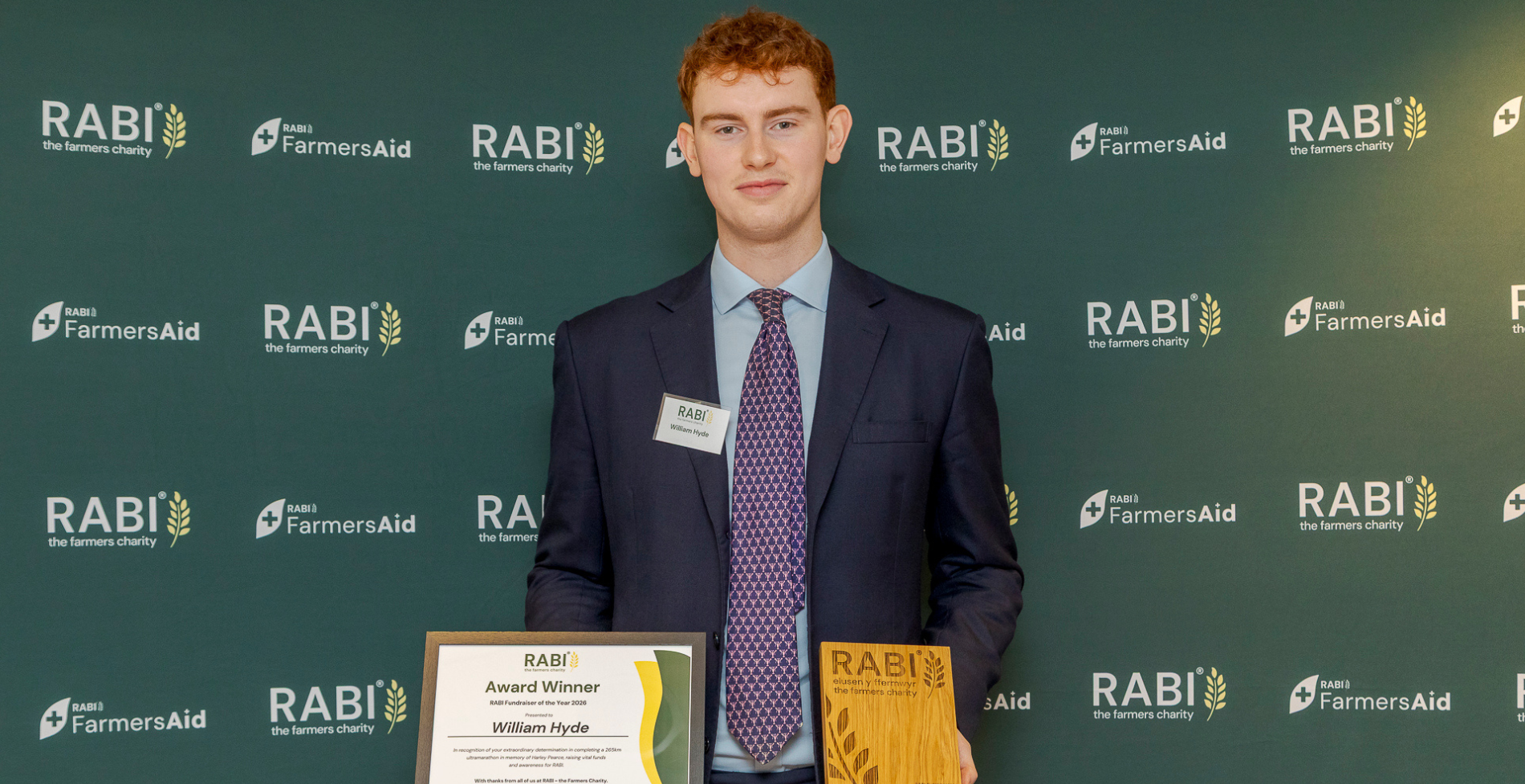 William Hyde holding his RABI Fundraiser of the Year 2026 trophy and certificate, standing in front of RABI and FarmersAid branding.